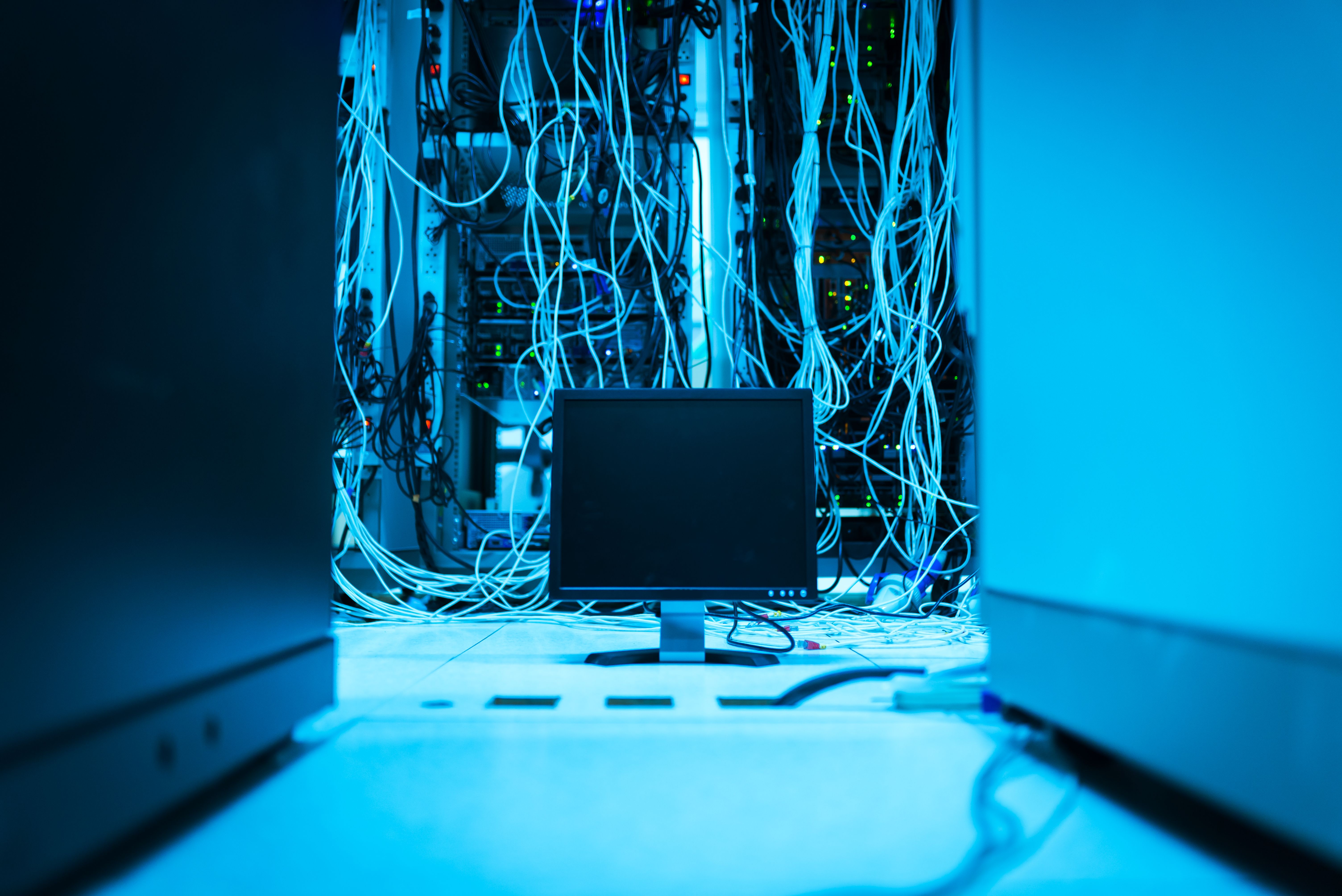 Network cabling and a monitor inside a server rack lit in blue